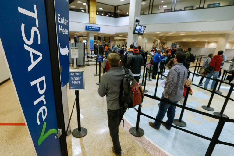 Traveler with backpack waits in line at an airport security checkpoint, surrounded by tall blue 'Enter Here' signs.